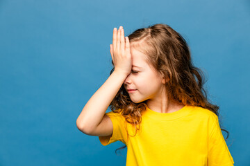 Frustrated beautiful caucasian little girl wearing yellow T-shirt over blue background holding hand...