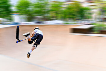 Young man practicing Scootering (Freestyle Scootering) in the new SkatePark in the central park of Igualada, Barcelona, Spain. blurred background	