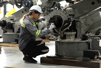 Industrial engineer working on robot maintenance in AI futuristic electronic technology factory. Female technician checking automated robotic machine. Modern smart woman empowerment in industry 4.0.