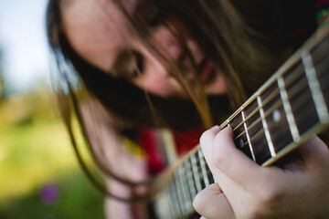A girl playing the guitar, with the focus on the chords and strings, her face softly blurred in the...