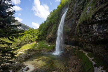 Fontanon of Goriuda, Udine. Wonderful waterfall that falls from a cliff. The force of the waterfall is a sight to behold. Hiking, trekking in the open area surrounded by woods. Summer holidays, peace.