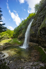 Fontanon of Goriuda, Udine. Wonderful waterfall that falls from a cliff. The force of the waterfall is a sight to behold. Hiking, trekking in the open area surrounded by woods. Summer holidays, peace.