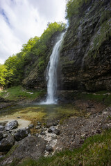 Fontanon of Goriuda, Udine. Wonderful waterfall that falls from a cliff. The force of the waterfall is a sight to behold. Hiking, trekking in the open area surrounded by woods. Summer holidays, peace.