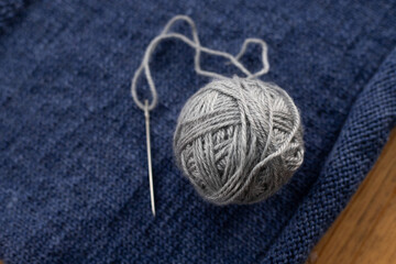 Knitting. Blue wool knitted fabric and a ball of gray thread with a needle for stitching details.
