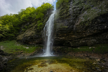 Fontanon of Goriuda, Udine. Wonderful waterfall that falls from a cliff. The force of the waterfall is a sight to behold. Hiking, trekking in the open area surrounded by woods. Summer holidays, peace.