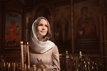 Young beautiful woman in the Orthodox Church lit candles in a candlestick