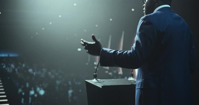 Portrait of an Empowering Thought Leader Standing at a Tribune, Showing an Inspiring Presentation About Innovation at Technology Conference. African Man Talking to an Audience in a Dark Venue