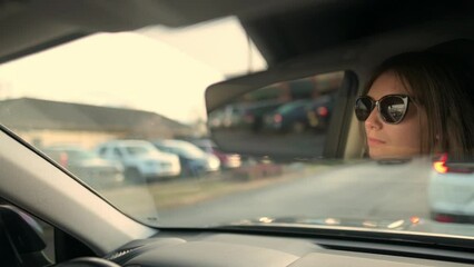 A woman driver is captured in the rearview mirror, focused on the road ahead during a traffic jam, illustrating everyday commuting challenges and concentration while driving