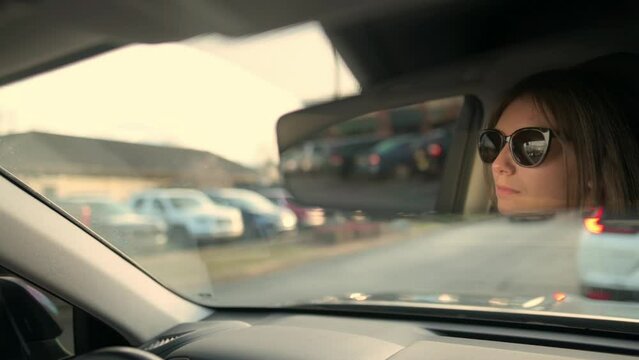 A woman driver is captured in the rearview mirror, focused on the road ahead during a traffic jam, illustrating everyday commuting challenges and concentration while driving