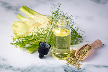 A bottle of fennel essential oil with fresh green fennel twigs and fennel seeds in the background