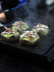hamburguesas de carne de ternera, queso fundido y beicon friéndose a la plancha