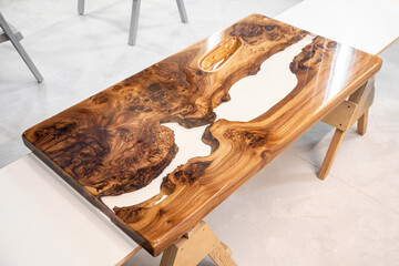 Live edge elm burl slab table top with central epoxy resin river on sawhorses in professional workshop