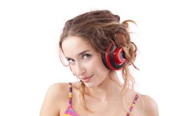 Portrait of young smiling woman who is listening to music through red headphones, looks into the camera with her blue eyes, while being isolated on a white background
