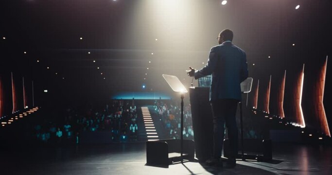 Confident Thought Leader Walking to a Tribune with laptop Computer, Delivering an Inspiring Presentation About Innovation at Technology Conference. Black Man Talking to an Audience in a Dark Venue