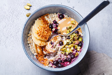 Overnight oatmeal with black currants, pistachios, coconut crumbs and peanut butter, gray background.