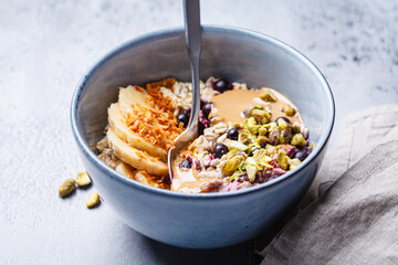 Overnight oatmeal with black currants, pistachios, coconut crumbs and peanut butter, gray background.