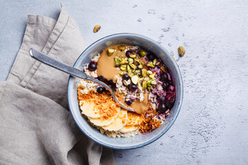 Overnight oatmeal with black currants, pistachios, coconut crumbs and peanut butter, gray background.