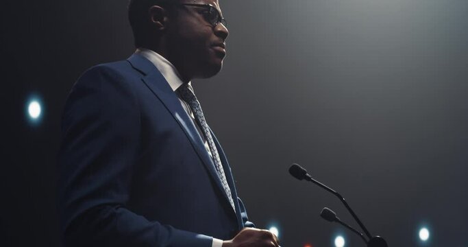 Portrait of an Energetic Speaker Giving a Speech at a Modern Conference Hall in Front of Crowd of Corporate Specialists. Handsome Black Presenter Motivating Young Leaders and Business Experts