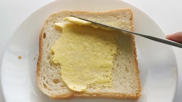 Butter on bread on a white plate. A knife spreading butter on bread.