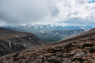 Dramatic top view from stone pass above alpine valley to large mountain range with snow-capped...