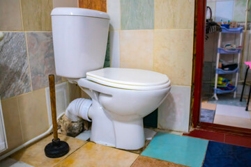 A serviceman is repairing a toilet with a hand plunger caused by a clogged toilet.