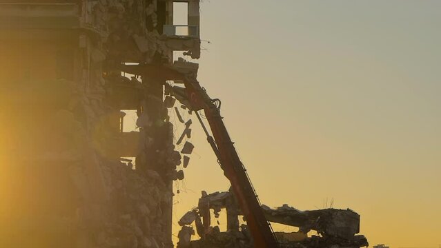 Excavator with hydraulic crusher is tearing down the old typical Turkish multi-storey apartment, residential building in Istanbul, Turkey at sunset - demolition of building: slow motion, backlight