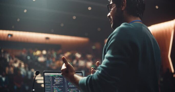 Portrait of a Young Speaker Standing on a Conference Stage. Technology Startup Founder Using a Laptop Computer, Speaking About Software Integration at a Business Meeting with Professional Audience