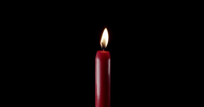 A single red candle burning. Isolated candle burning with dark background. Red paraffin candle with yellow shades burns on a black background. Background or illustration of remembrance or celebration.