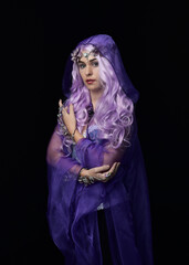 artistic portrait of beautiful female model with long purple hair wearing a flowing fantasy cloak.  isolated on dark studio background.