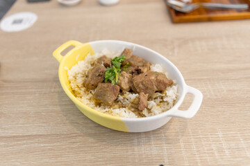 Baked pork rice with garlic sauce in a ceramic bowl on a wooden table in a restaurant.