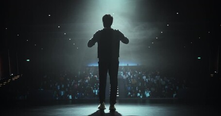 Cinematic Footage of an Anonymous Man Standing Under a Spotlight on Stage in Front of a Sold-Out Audience. Motivational Speaker or a Stand Up Comedian Making an Unforgettable Performance