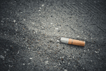 Cigarette butts on the sand with shell fragments on the beach have a negative effect on the marine environment in dark black tone background.