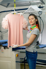 professional dry cleaning young girl irons pink sweater on a hanger with steam look on camera