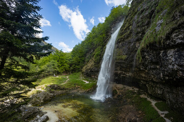Fototapeta premium Fontanon of Goriuda, Udine. Wonderful waterfall that falls from a cliff. The force of the waterfall is a sight to behold. Hiking, trekking in the open area surrounded by woods. Summer holidays, peace.