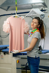 professional dry cleaning young girl irons pink sweater on a hanger with steam look on camera