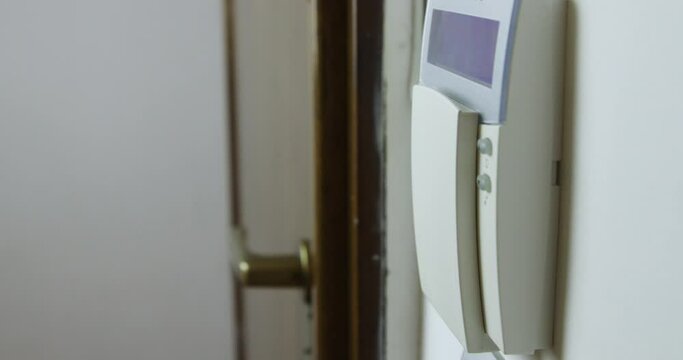 A mans hand is captured as he sets an alarm on a wall-mounted security keypad inside a house, ensuring safety and security.