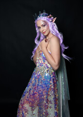 artistic portrait of beautiful female model with long purple hair and elf ears, wearing a fantasy fairy crown, wearing a rainbow glitter sequin ball gown. Standing in side profile, isolated on dark st