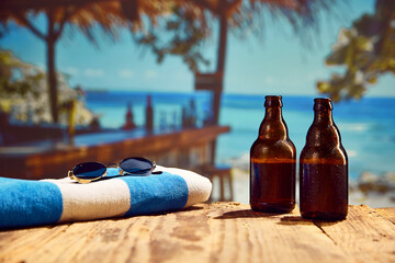 Beachside relaxation. Sunglasses, towel and cold beer bottles standing on a wooden table on beach...