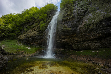 Fontanon of Goriuda, Udine. Wonderful waterfall that falls from a cliff. The force of the waterfall is a sight to behold. Hiking, trekking in the open area surrounded by woods. Summer holidays, peace.