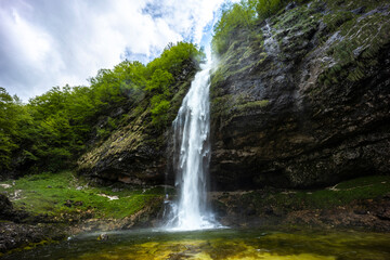 Fototapeta premium Fontanon of Goriuda, Udine. Wonderful waterfall that falls from a cliff. The force of the waterfall is a sight to behold. Hiking, trekking in the open area surrounded by woods. Summer holidays, peace.