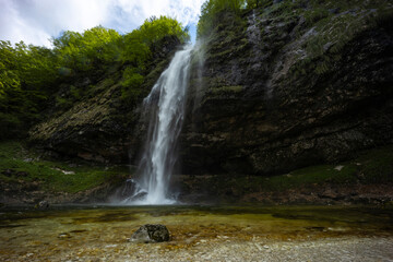 Fototapeta premium Fontanon of Goriuda, Udine. Wonderful waterfall that falls from a cliff. The force of the waterfall is a sight to behold. Hiking, trekking in the open area surrounded by woods. Summer holidays, peace.