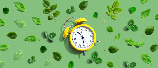 Yellow vintage alarm clock with green leaves - flat lay
