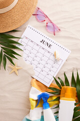 Flat lay of June calendar surrounded by summer vacation essentials on a sandy texture, perfect for holiday planning guides