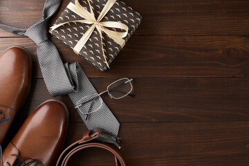 Flat lay of elegant Father's Day gifts including a stylish tie, glasses, and gift boxes on a dark wooden background, perfect for use in retail marketing or social media campaigns