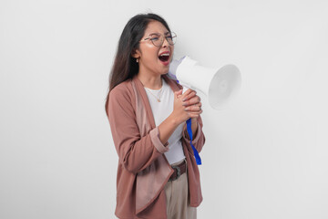 Young Asian woman wearing cardigan and eyeglasses shouting at megaphone, isolated on white...