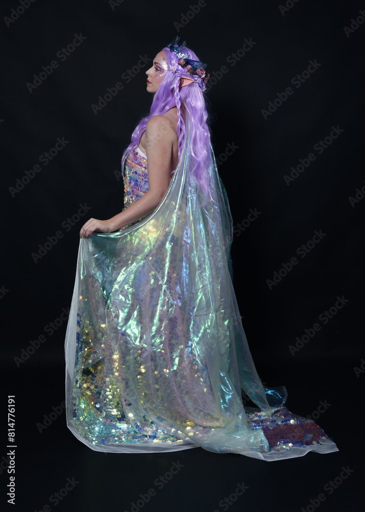 Sticker Full length portrait of beautiful female model with long purple hair wearing elf ears, a fantasy fairy crown and  rainbow glitter sequin ball gown.  walking away, back view, isolated dark studio 