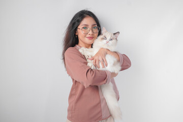 Lovely Asian woman wearing eyeglasses holding her ragdoll cat and smiling to the camera isolated over white background.