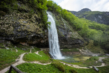 Fontanon of Goriuda, Udine. Wonderful waterfall that falls from a cliff. The force of the waterfall is a sight to behold. Hiking, trekking in the open area surrounded by woods. Summer holidays, peace.