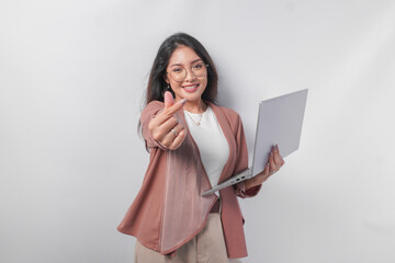Cute young business Asian woman holding a laptop making finger heart shape over isolated white background.