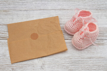 Pink baby booties with paper on weathered wood